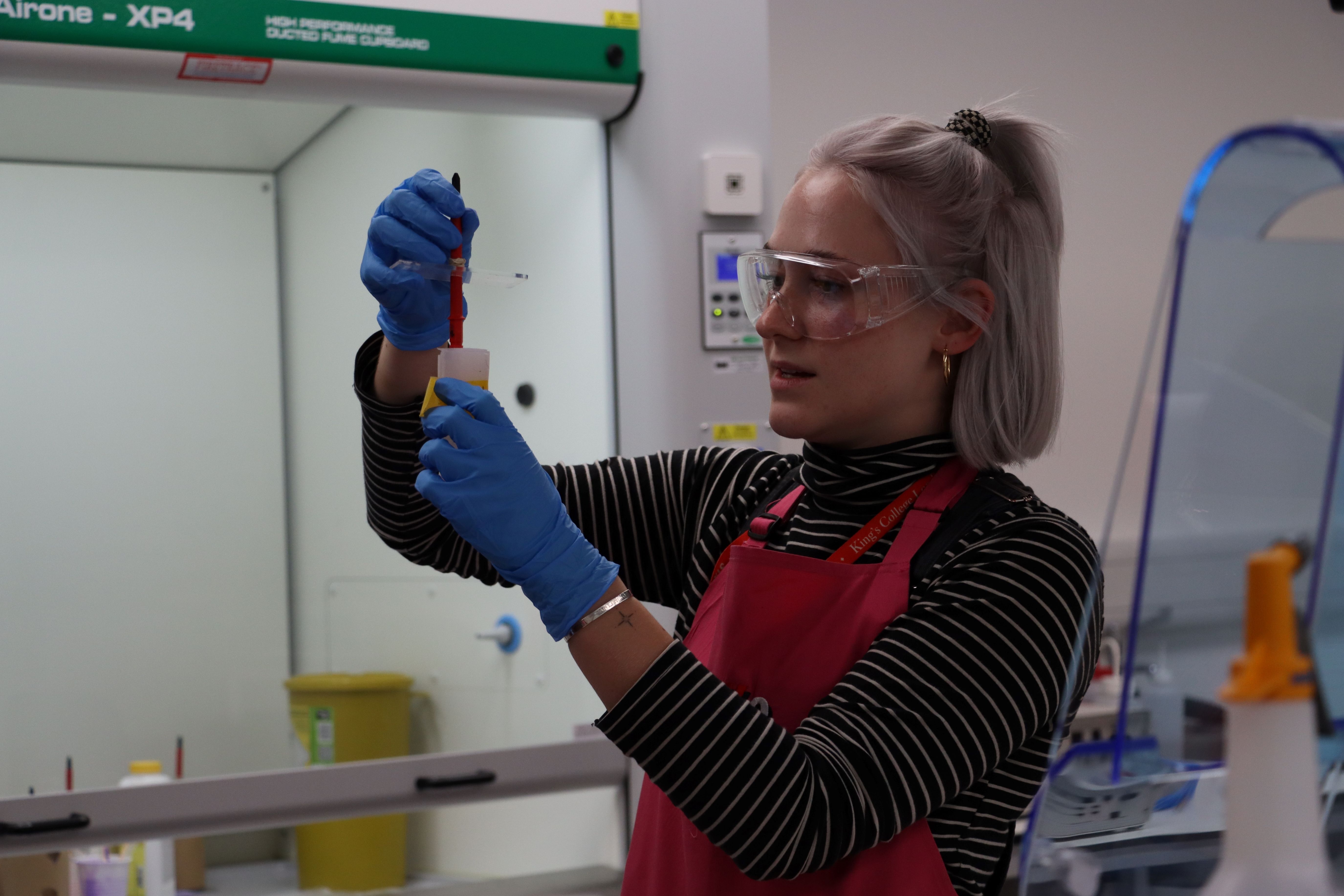 Charlotte Palmer,  Technical Manager (Makerspace) for the Engineering Department at King’s College London, works in a laboratory fume cupboard, carefully transferring a liquid sample using a pipette. Wearing safety goggles and gloves, she carries out precise experimental procedures that support engineering research and student laboratory teaching.