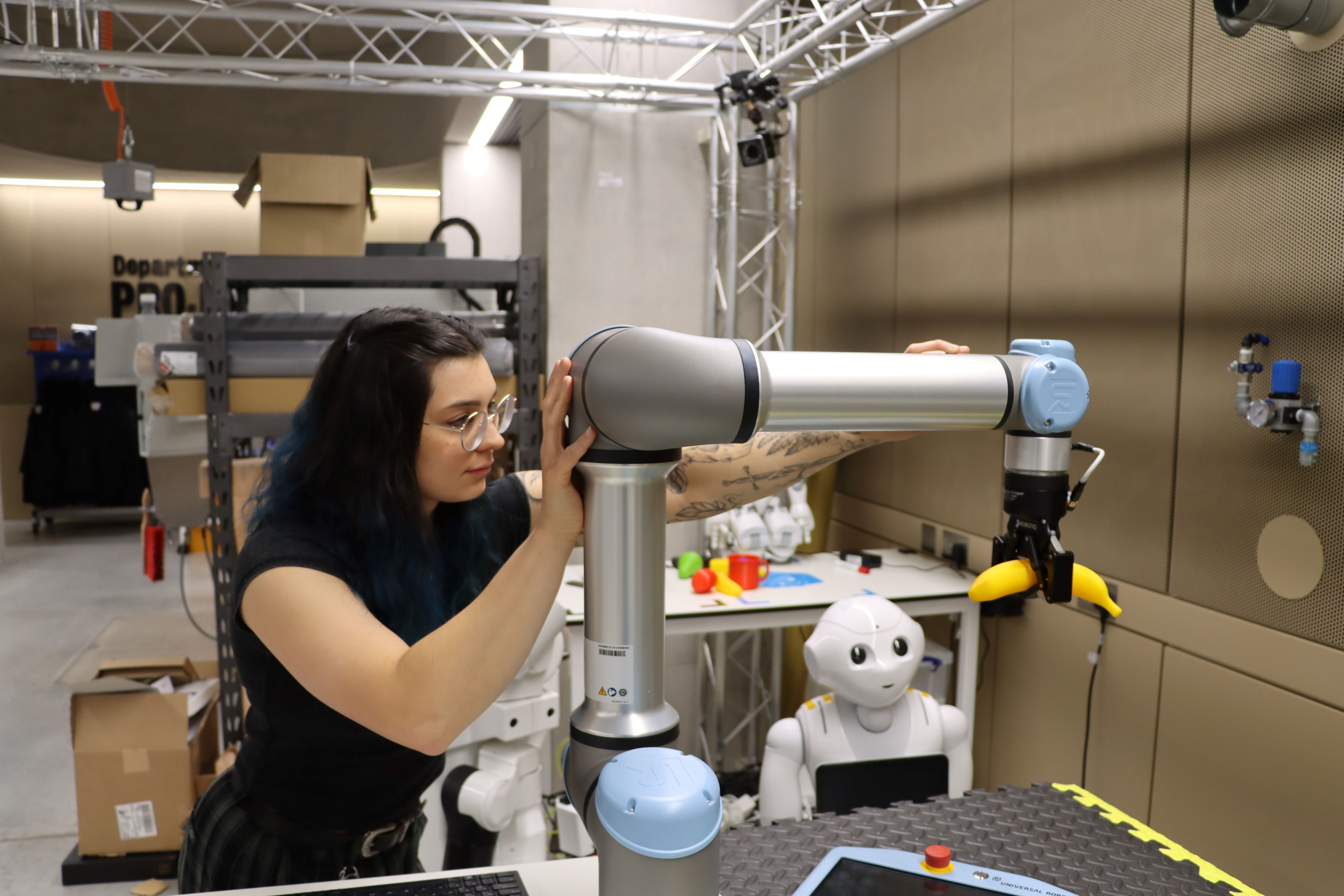 Ana Rubio Denniss, Senior Makerspace Technician, King’s College London, stands in a makerspace workshop, carefully adjusting a collaborative robotic arm as it grips a bright yellow object. Surrounded by robotics equipment and prototyping tools, she supports hands-on experimentation and innovation with advanced technologies.