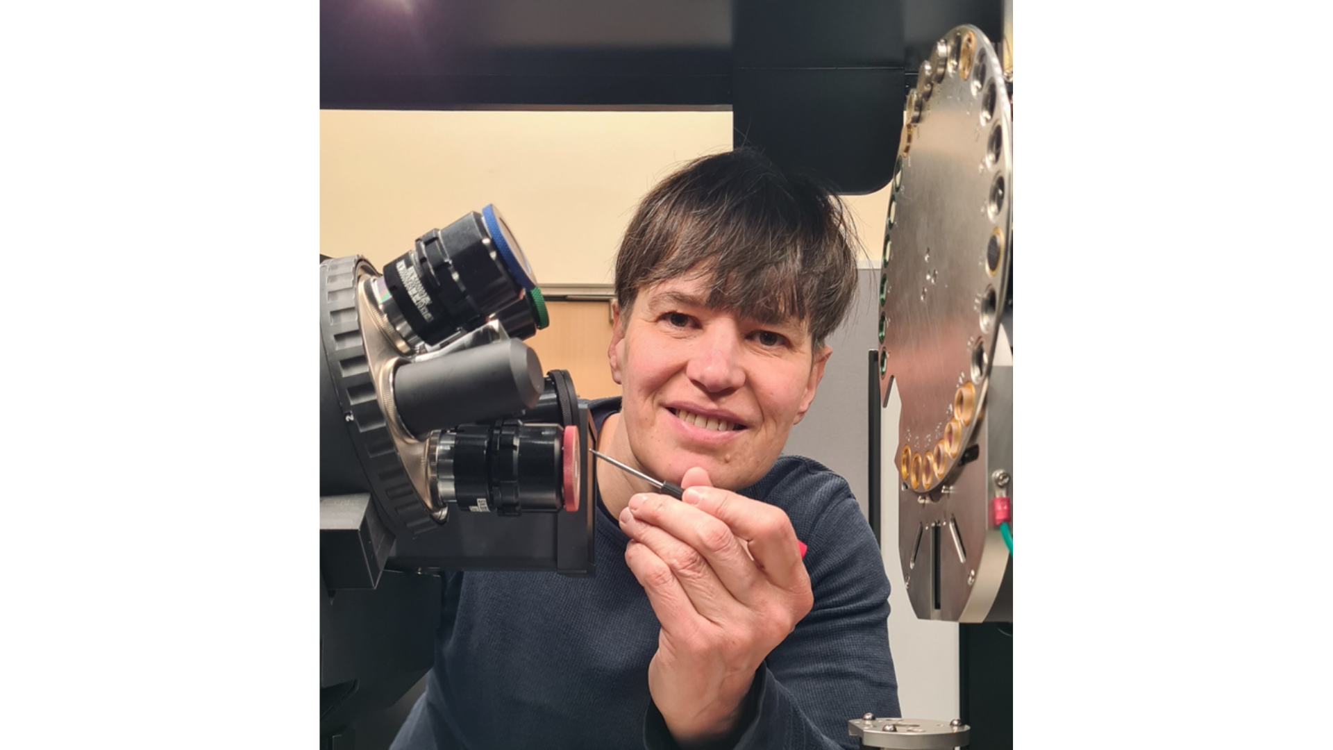 Dr Julia Behnsen, Research Technical Professional (X-ray micro-CT), University of Liverpool, leans beside a specialised X-ray micro-CT instrument, carefully adjusting part of the equipment with a precision tool. Focused and hands-on, she works with advanced imaging technology used to generate detailed three-dimensional scans of materials and biological samples.