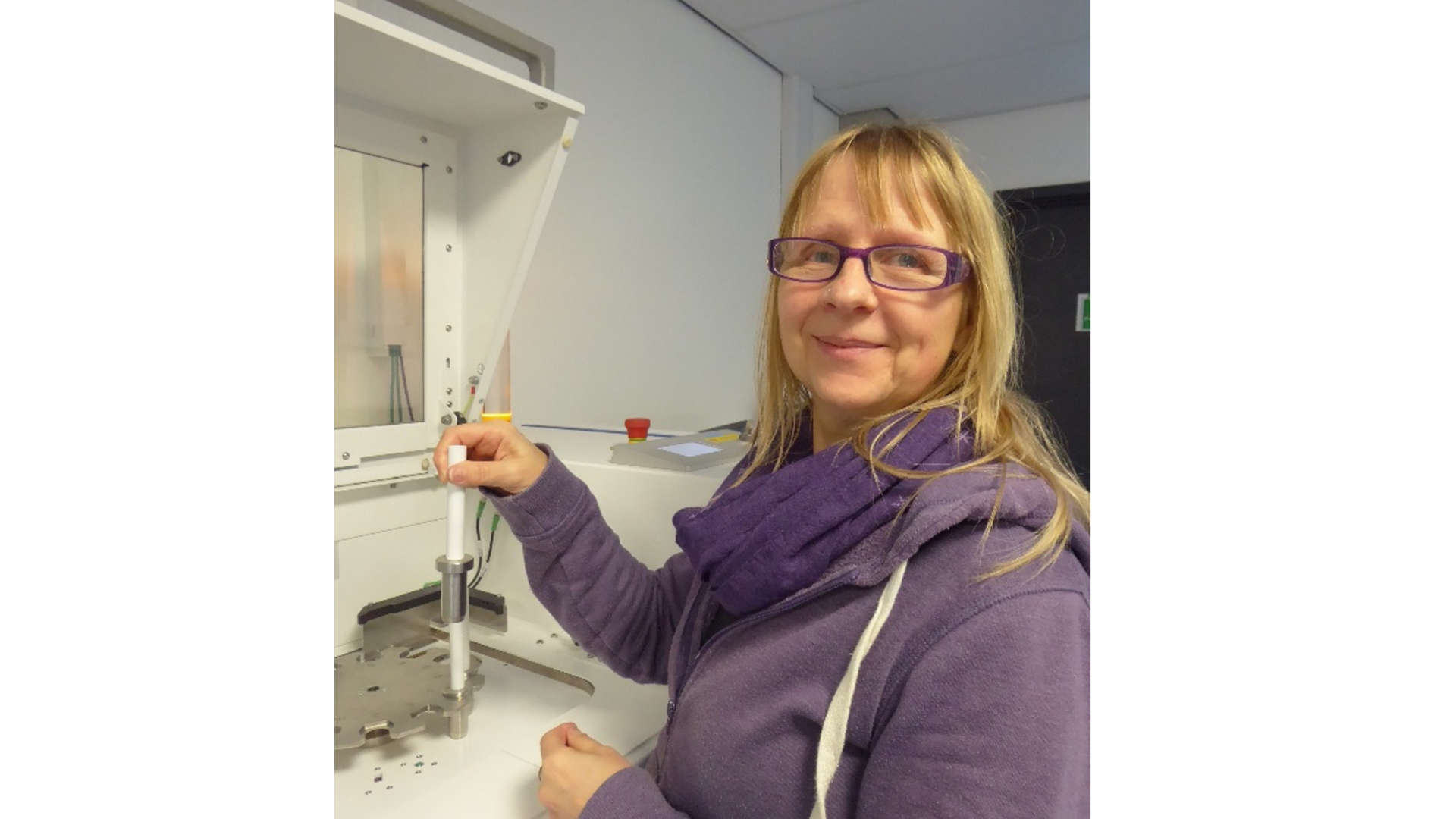 Karen Askew, a research technician at IBERS, stands beside a specialised laboratory instrument, smiling as she carefully positions a sample holder within the machine. Working with analytical equipment used to study plant or soil samples, she carries out precise technical procedures that support agricultural and environmental research.