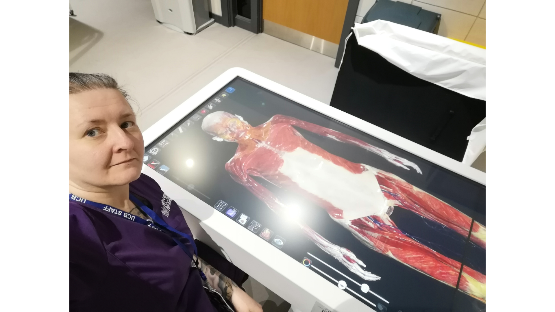 Michelle Deakin, Clinical Skills and Simulation Technician, University College Birmingham, stands beside a large interactive anatomy table displaying a detailed digital model of the human body. Using advanced simulation technology, she supports healthcare education by helping students explore anatomical structures and develop practical clinical skills in a realistic learning environment.