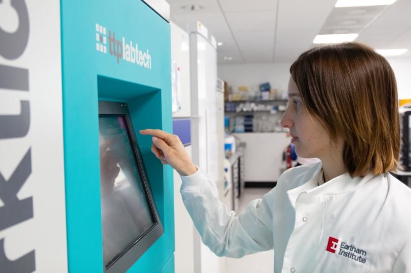 a young technician in an Earlham Institute lab coat working at a screen