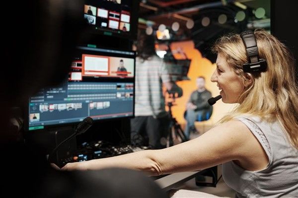 Rebecca Russell Cooper, Production Lead at the University of Leeds, sits at a broadcast control desk wearing a headset, monitoring multiple screens while operating video production software during a live studio recording. Focused on the controls in front of her, she coordinates the technical elements of filming and streaming, supporting professional media production in a university setting.