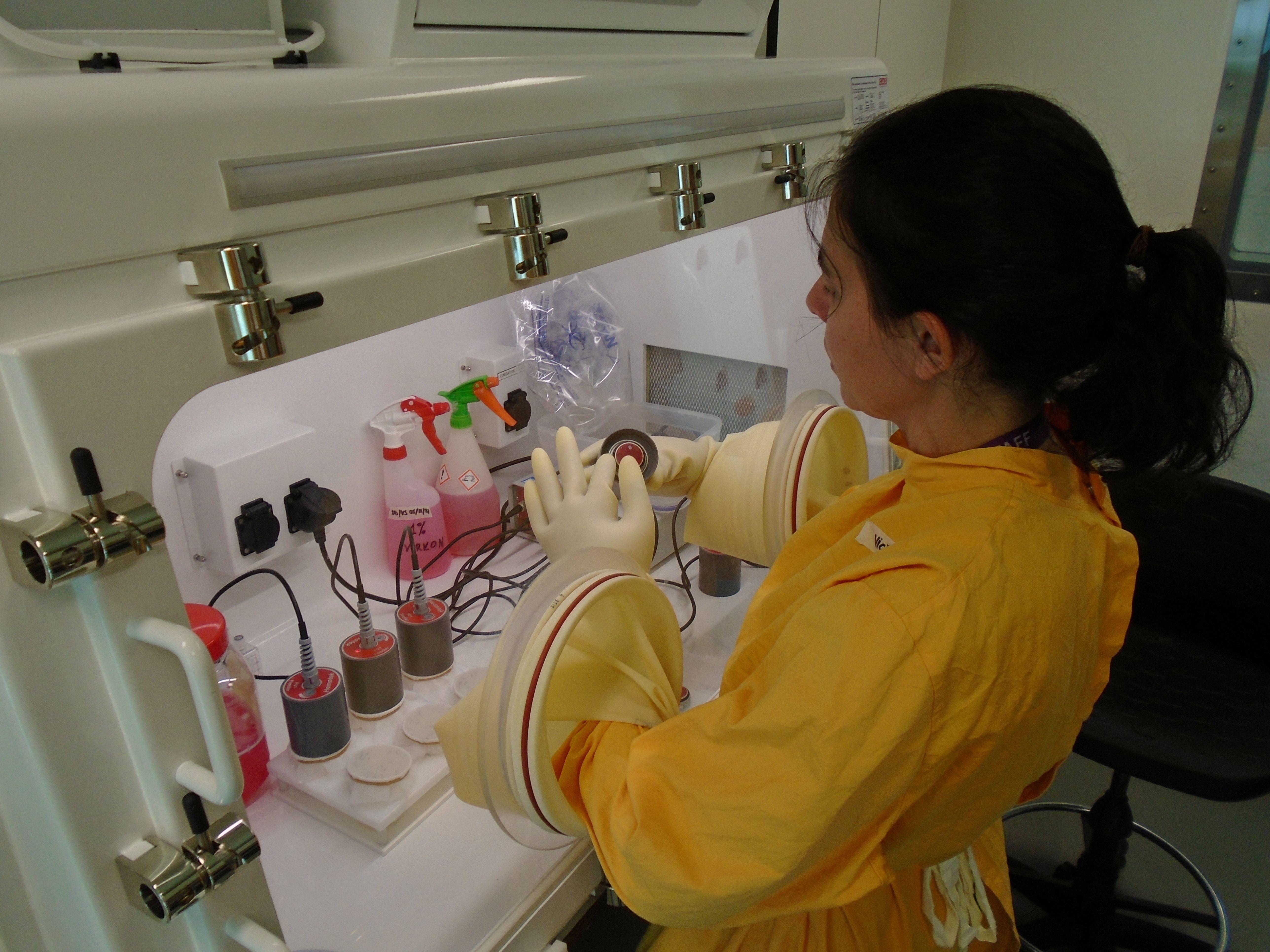 Dr. Victoria Sy, a Postdoctoral Scientist working within the CL3 Virology Science Technology Platform at The Pirbright Institute, works at a sealed laboratory glove box, wearing a yellow protective suit as she carefully handles samples through built-in gloves. Surrounded by specialised containment equipment and monitoring devices, she carries out precise laboratory work required for safely studying viruses in a high-containment research environment.